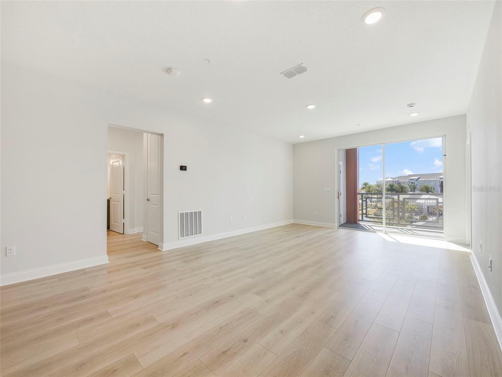 An empty living room with light wood-look flooring, recessed lighting, and a sliding glass balcony door — 7545 LAUREATE BOULEVARD UNIT 7301, ORLANDO, FL