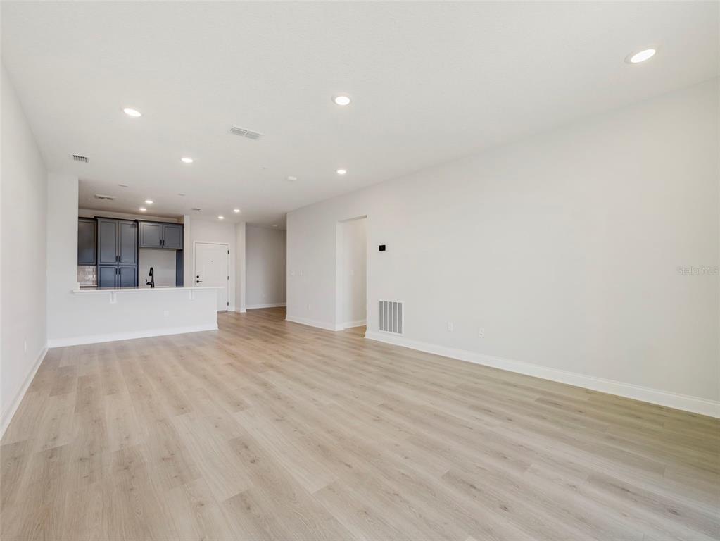 An open-concept living area features light wood-look flooring and a view into a kitchen — 7545 LAUREATE BOULEVARD UNIT 7301, ORLANDO, FL