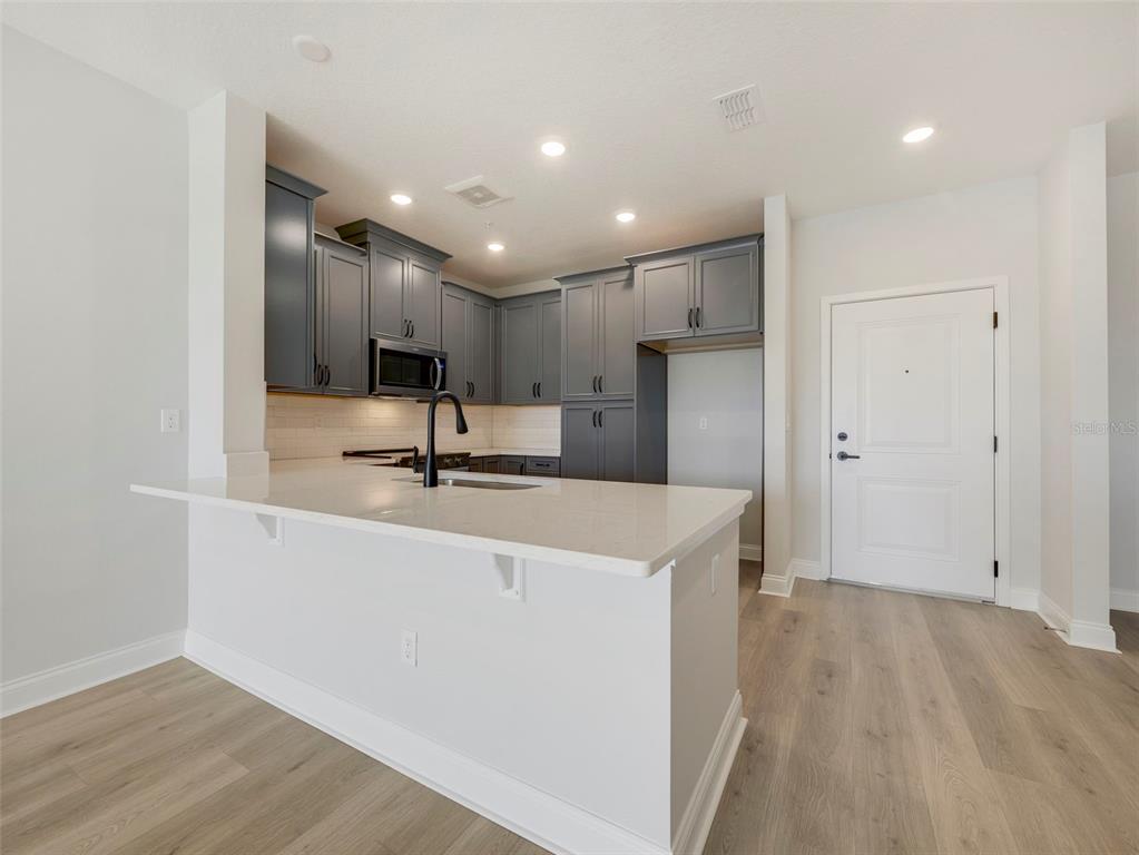 A kitchen features dark gray cabinets, white countertops, a breakfast bar, and light wood flooring — 7545 LAUREATE BOULEVARD UNIT 7301, ORLANDO, FL