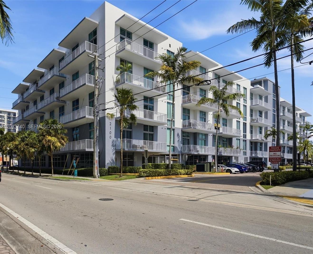 A multi-story modern apartment building with white balconies and palm trees sits along a street — 2100 Van Buren St # 322, Hollywood FL 33020, HOLLYWOOD, FL