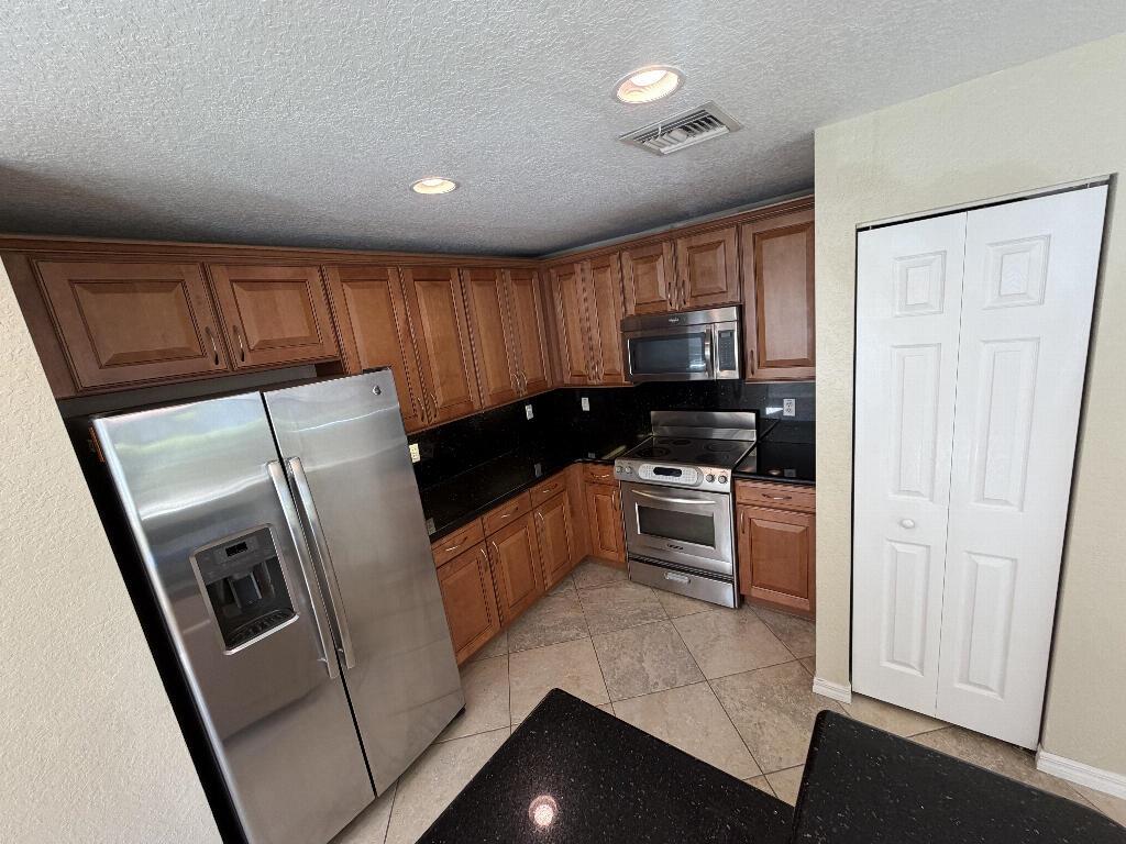 A kitchen with wood cabinets, black countertops, stainless steel appliances, and tile flooring — 22159 Majestic Woods Way, Boca Raton FL 33428, BOCA RATON, FL