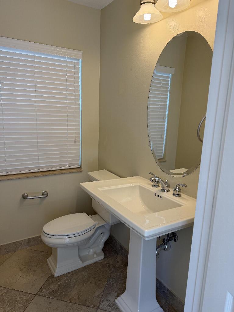 A bathroom features a pedestal sink, an oval mirror, a toilet, and tile flooring — 22159 Majestic Woods Way, Boca Raton FL 33428, BOCA RATON, FL