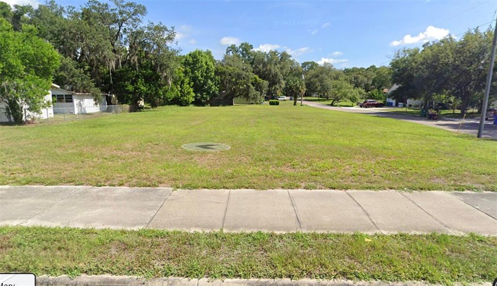 A vacant, grassy residential lot sits between a white house and a paved street — 130 N HOLLIS STREET, LAKE MARY, FL