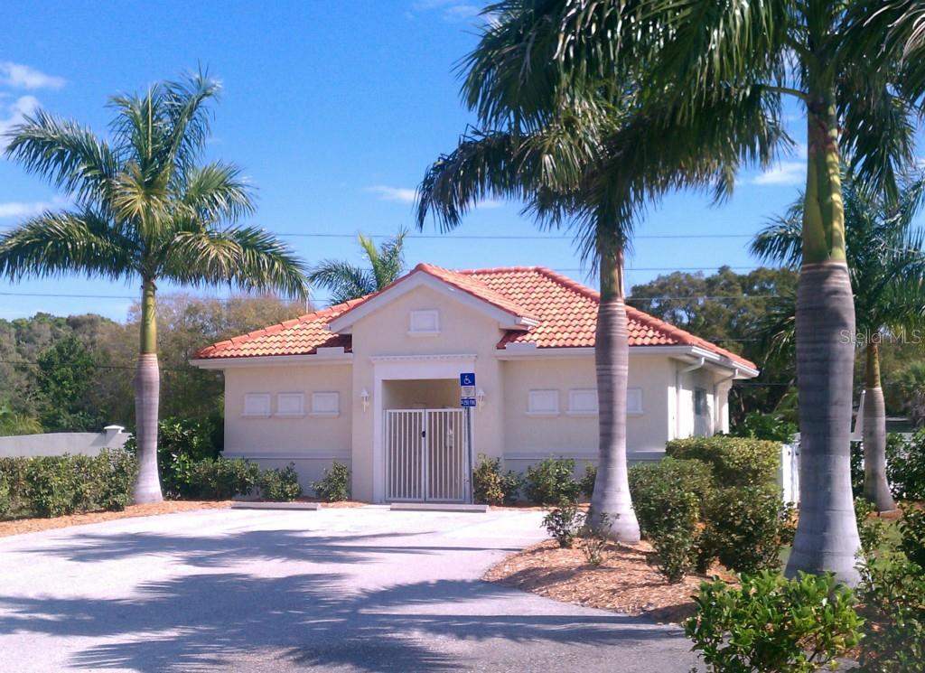 A small, light-colored building with a tiled roof stands behind palm trees and a parking area — 10313 HEBBLEWHITE COURT, ENGLEWOOD, FL