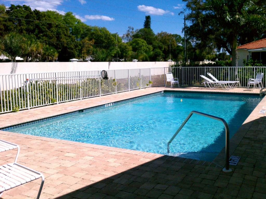 A rectangular swimming pool with a paver deck is enclosed by a white metal fence — 10313 HEBBLEWHITE COURT, ENGLEWOOD, FL