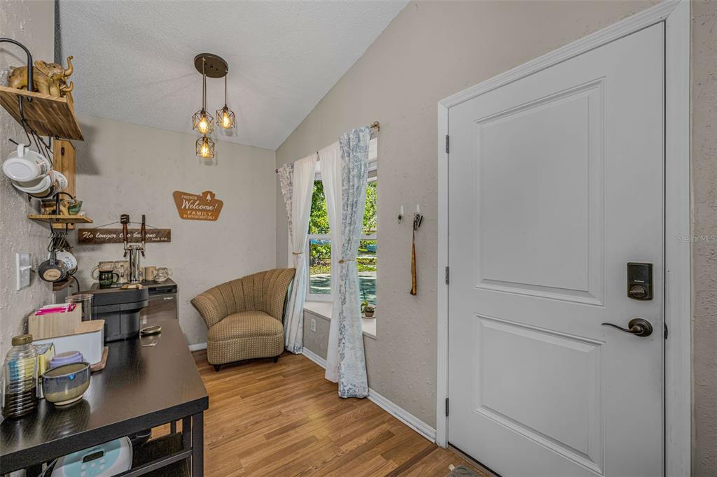 An entryway features wood-look flooring, a coffee station, a patterned armchair, and a white door — 2662 MEGAN COURT, PALM HARBOR, FL
