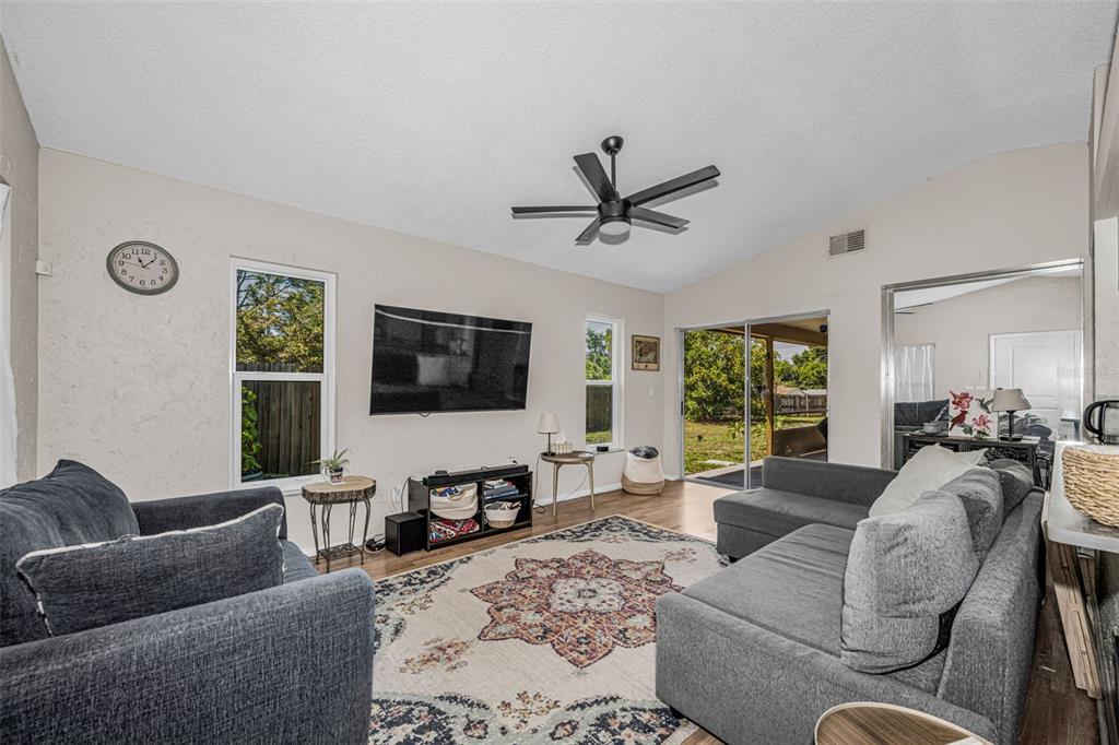 A living room features gray sofas, a patterned rug, a wall-mounted television, and sliding doors — 2662 MEGAN COURT, PALM HARBOR, FL