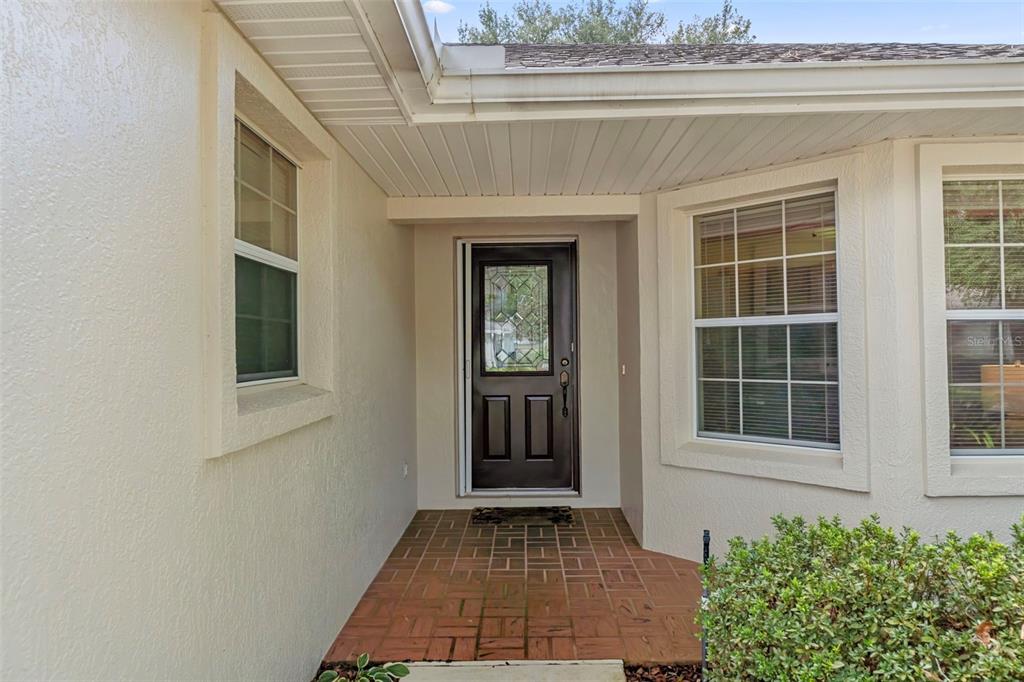 A covered entryway features a dark front door, brick flooring, and two adjacent windows — 6482 W TORRINGTON COURT, CRYSTAL RIVER, FL