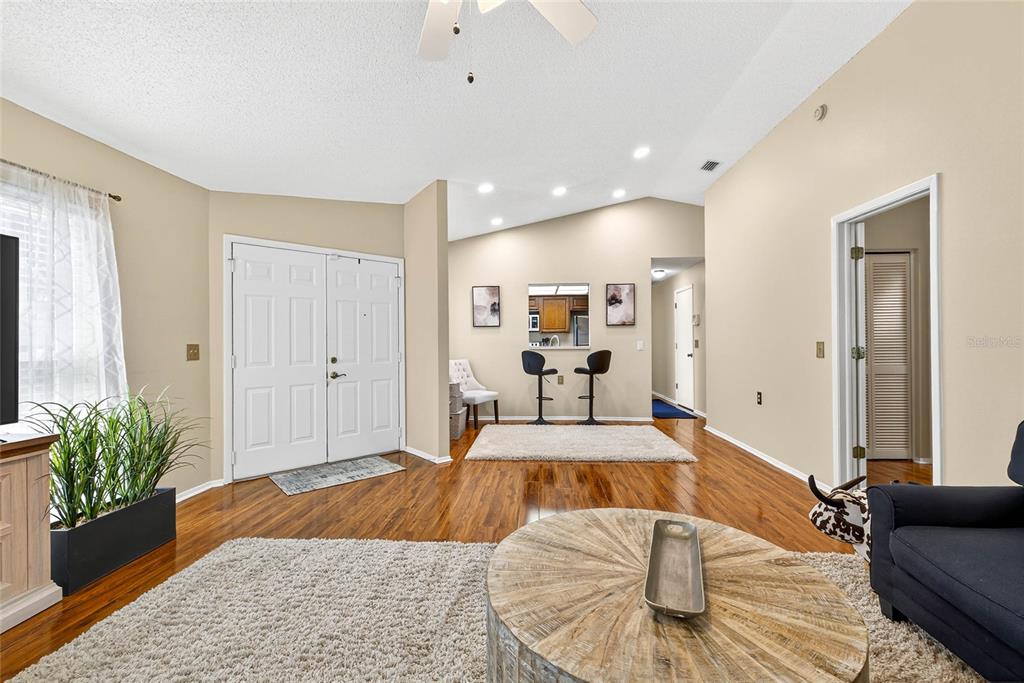 A living room with hardwood floors, a vaulted ceiling, and a pass-through window to the kitchen — 4658 WALLINGFORD COURT, NEW PORT RICHEY, FL