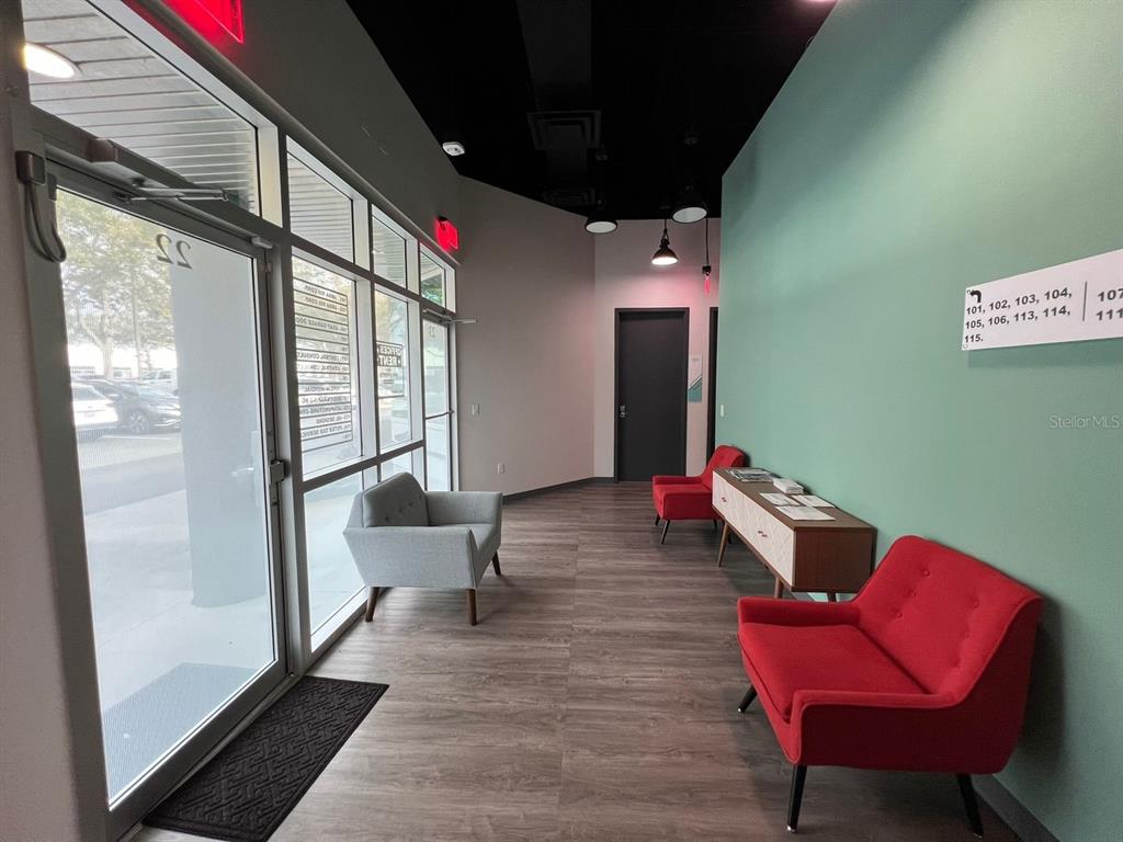 A modern office lobby features wood-look flooring, a teal accent wall, and red seating — 7362 FUTURES DRIVE UNIT 22, ORLANDO, FL