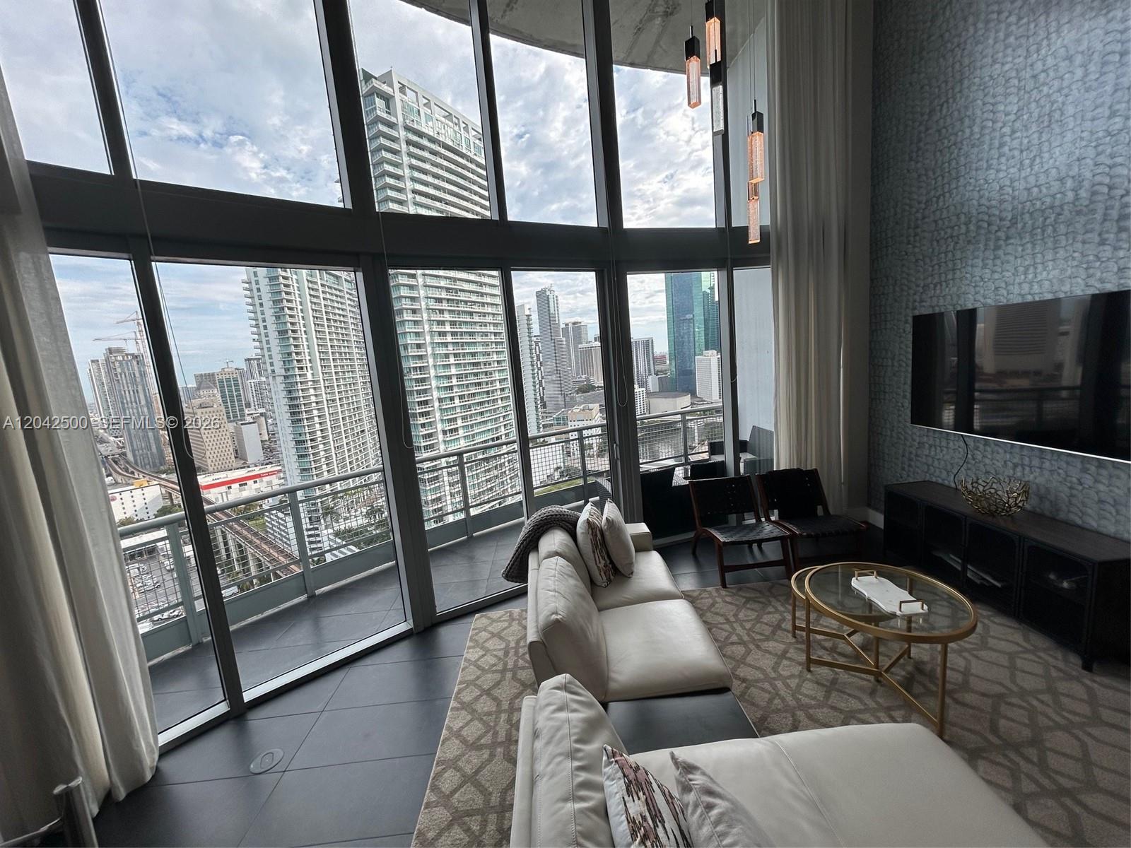 A modern living room features floor-to-ceiling windows with a view of high-rise city buildings — 690 SW 1st Ct # 3101, Miami FL 33130, MIAMI, FL