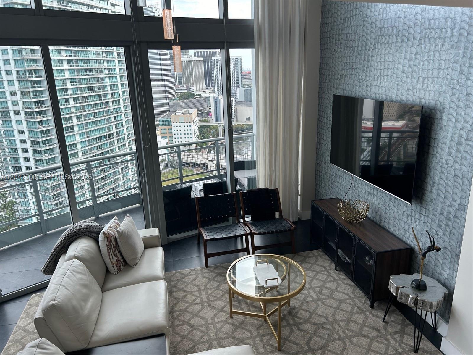 A modern living room features a white sofa, glass coffee table, and city skyline views — 690 SW 1st Ct # 3101, Miami FL 33130, MIAMI, FL