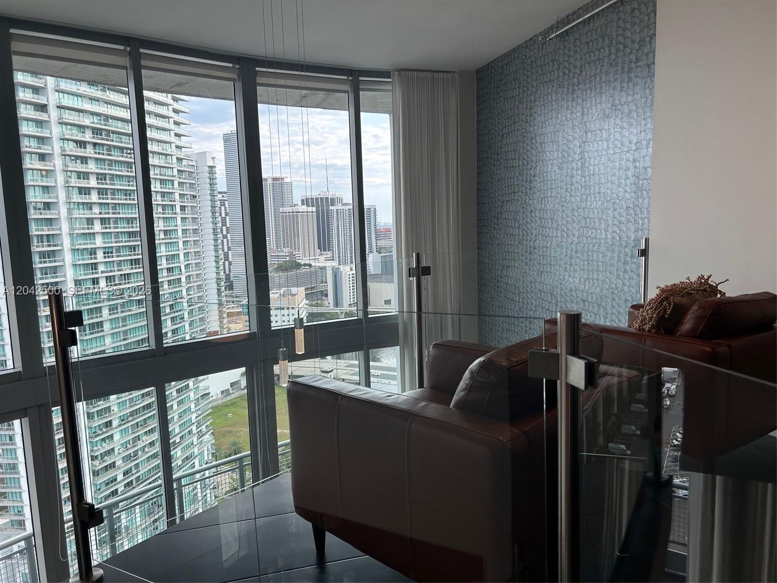 A modern living area features leather furniture, a glass railing, and floor-to-ceiling city views — 690 SW 1st Ct # 3101, Miami FL 33130, MIAMI, FL