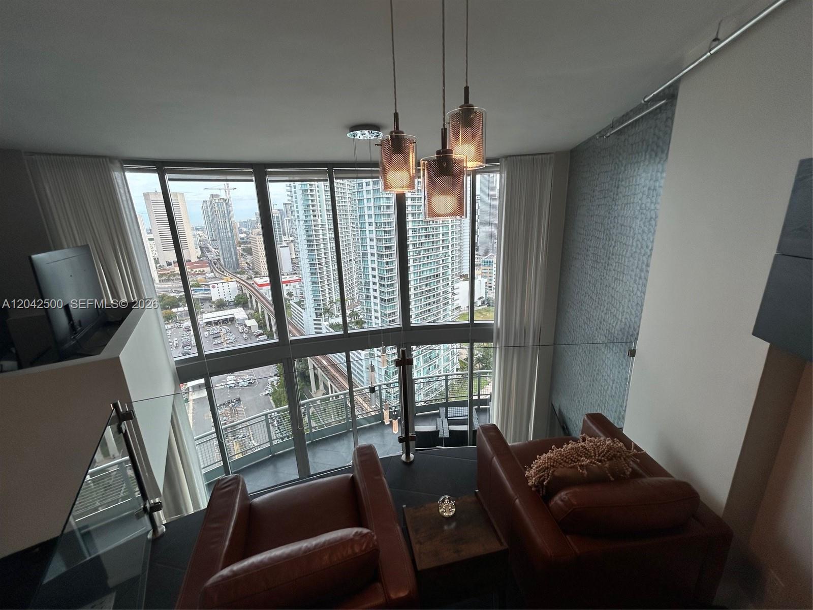A high-rise apartment living area features two leather armchairs, pendant lighting, and floor-to-ceiling windows — 690 SW 1st Ct # 3101, Miami FL 33130, MIAMI, FL