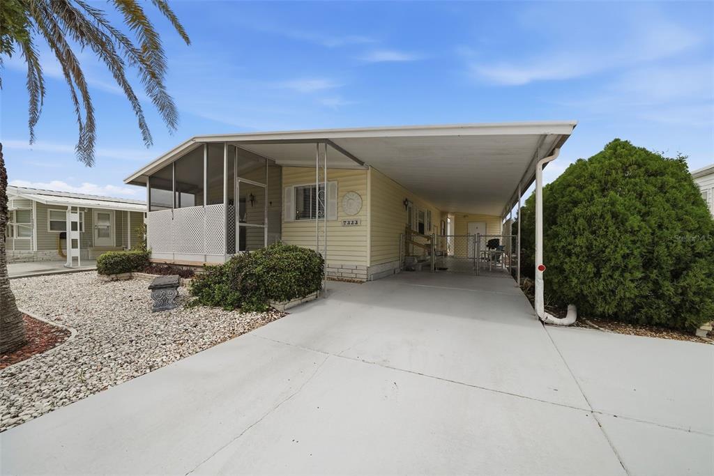 A yellow mobile home features a screened-in porch, a concrete driveway, and a covered carport — 7323 GRAND PINE DRIVE, HUDSON, FL