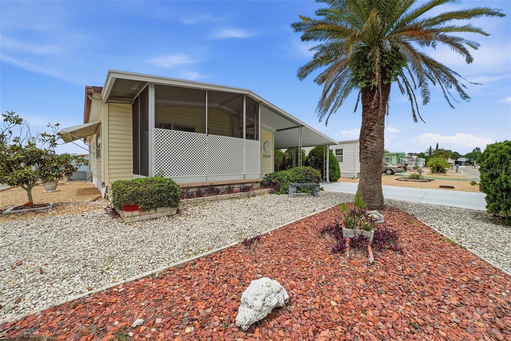 A light-colored mobile home features a screened-in porch, a palm tree, and gravel landscaping — 7323 GRAND PINE DRIVE, HUDSON, FL