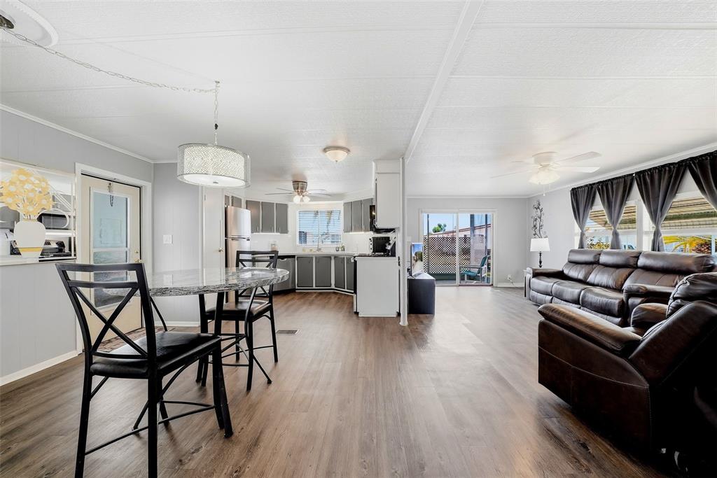 An open-concept living room and kitchen featuring wood-look flooring, dark leather furniture, and gray cabinetry — 7323 GRAND PINE DRIVE, HUDSON, FL