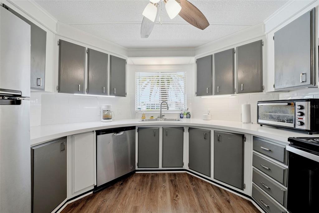 A kitchen features gray cabinets, white countertops, stainless steel appliances, and wood-look flooring — 7323 GRAND PINE DRIVE, HUDSON, FL