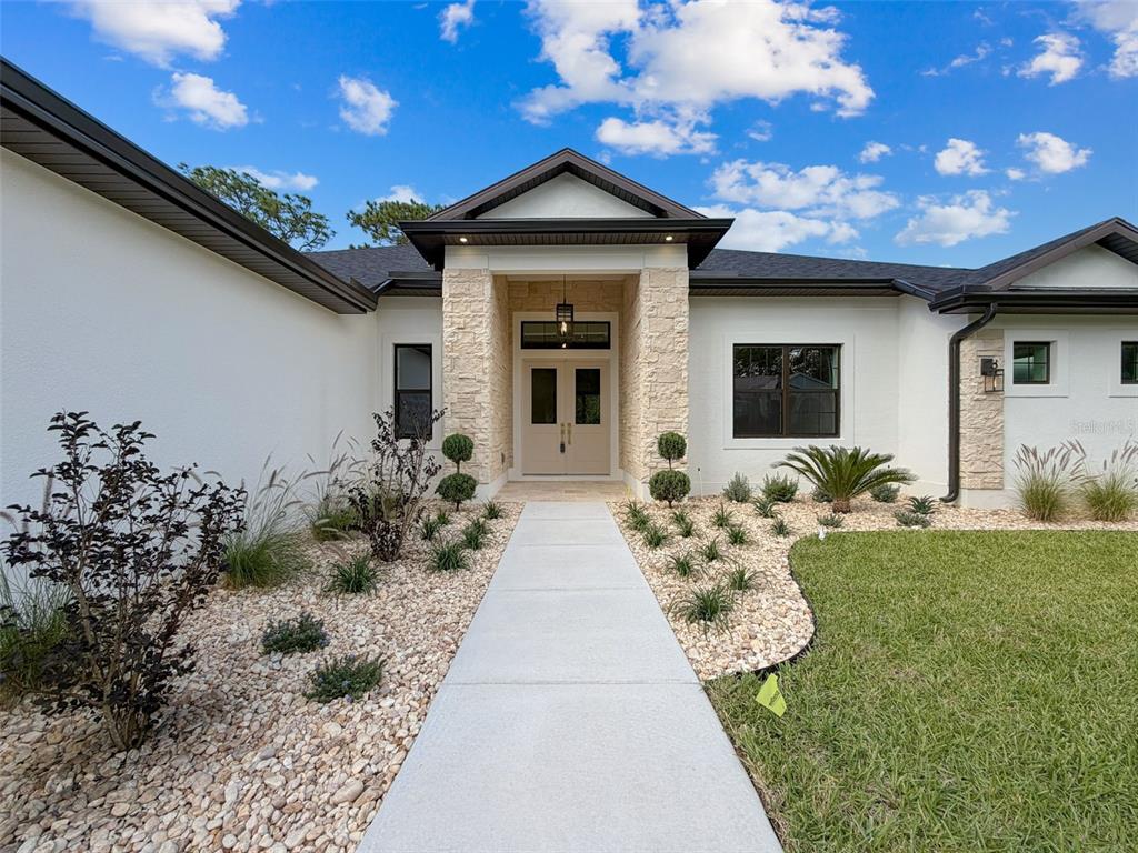 A concrete walkway leads to the stone-accented entryway of a white house with dark trim — 88 DAISY STREET, HOMOSASSA, FL