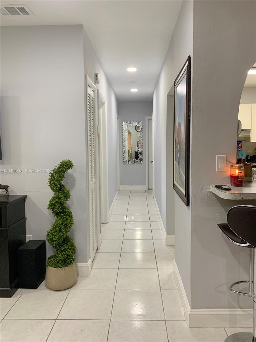 A hallway with white tile flooring leads past a potted topiary to a mirror — 8310 SW 37th St # 0, Miami FL 33155, MIAMI, FL