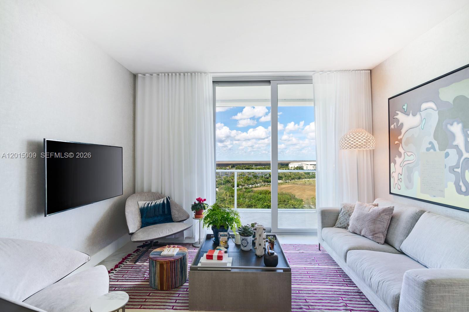 A living room features a sofa, armchair, coffee table, and a balcony with outdoor views — 2000 Metropica Way # 1207, Sunrise FL 33323, SUNRISE, FL