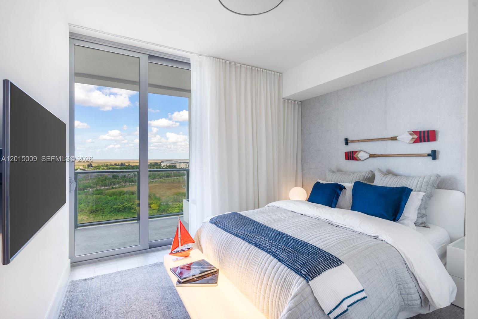 A bedroom features a bed with blue pillows, nautical decor, and a balcony with views — 2000 Metropica Way # 1207, Sunrise FL 33323, SUNRISE, FL