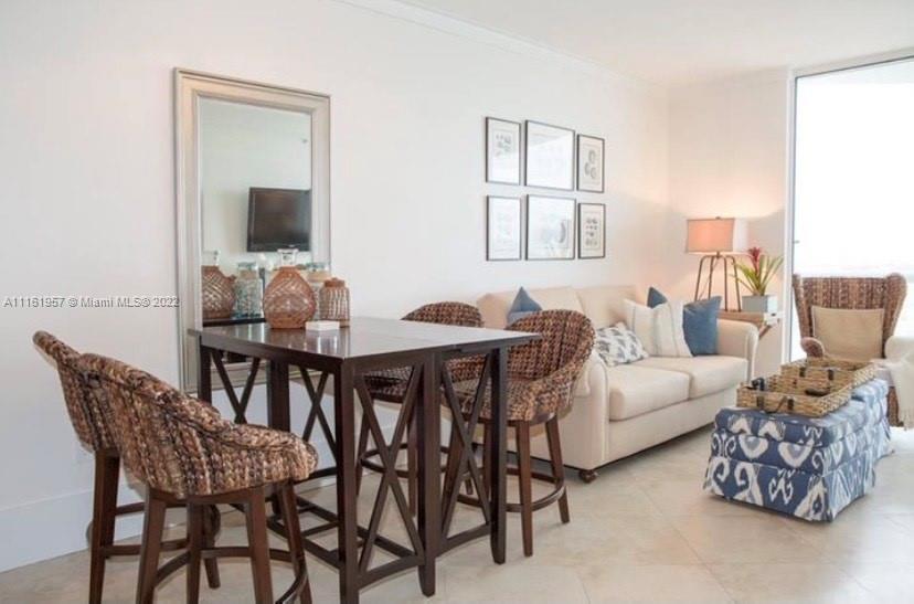A dining area with a wooden table and wicker chairs sits beside a beige sofa — 6365 Collins Ave # 2409, Miami Beach FL 33141, MIAMI BEACH, FL