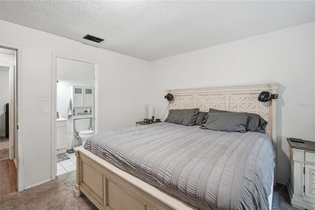 A bedroom features a large bed with a white headboard and an attached bathroom — 11505 PAPERWOOD PLACE, RIVERVIEW, FL