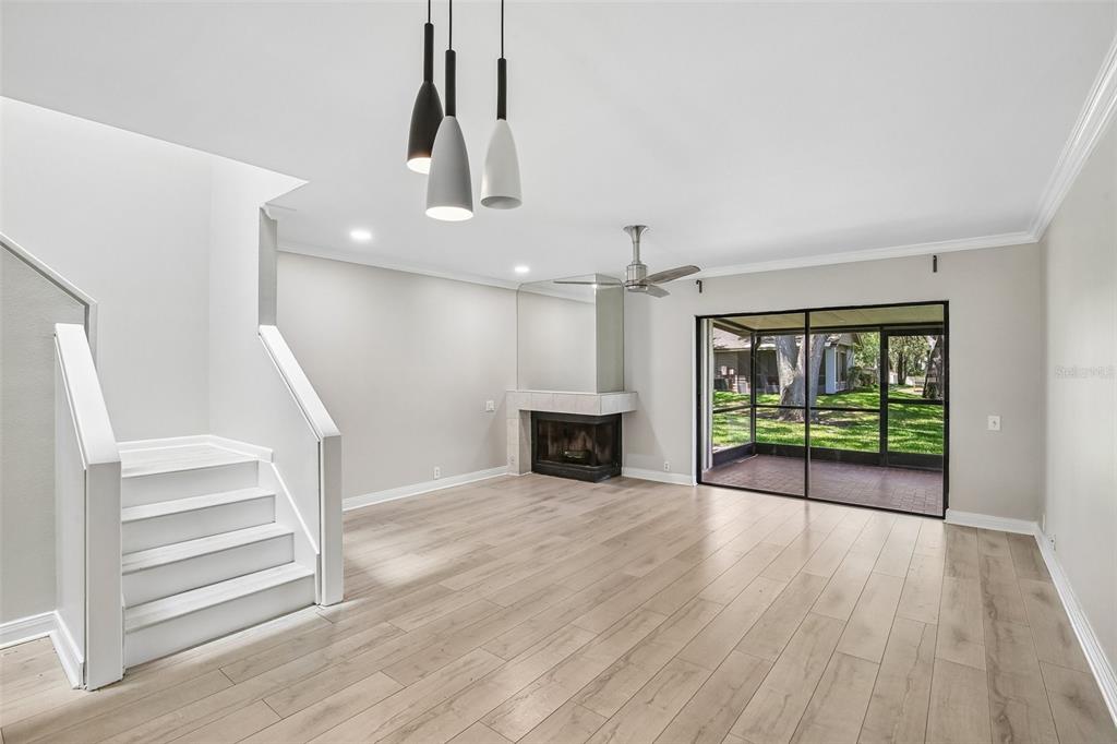 A living room with light wood flooring, a fireplace, a staircase, and sliding glass doors — 1006 CICERO LANE, BRANDON, FL