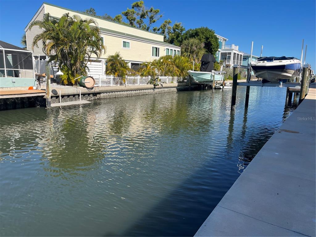 A canal view showing a yellow house, a boat lift, and a concrete dock — 701 SAINT JUDES DRIVE S UNIT 3, LONGBOAT KEY, FL