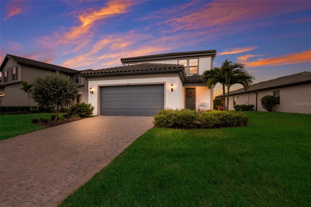 A two-story suburban house with a gray garage door and a paved driveway at sunset — 6072 BAYWOOD COURT, LAKEWOOD RANCH, FL