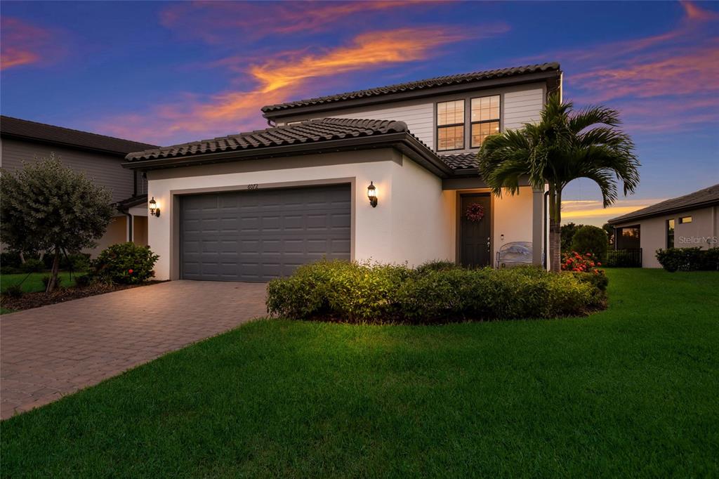 A two-story house with a gray garage, a paved driveway, and a palm tree at dusk — 6072 BAYWOOD COURT, LAKEWOOD RANCH, FL