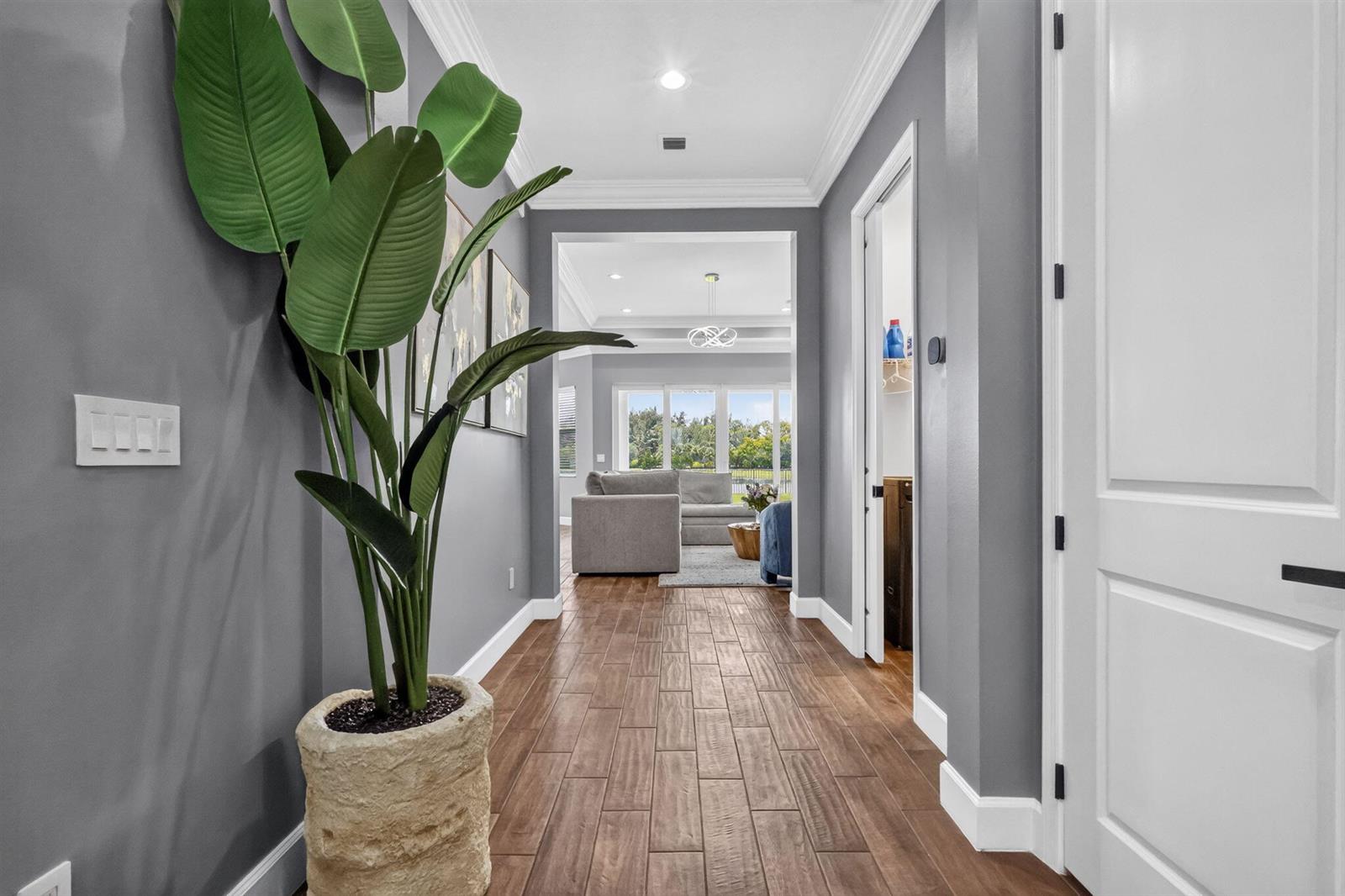 A hallway with wood-look tile flooring leads toward a living room with large windows — 15660 Goldfinch Circle, FL 33470, FL