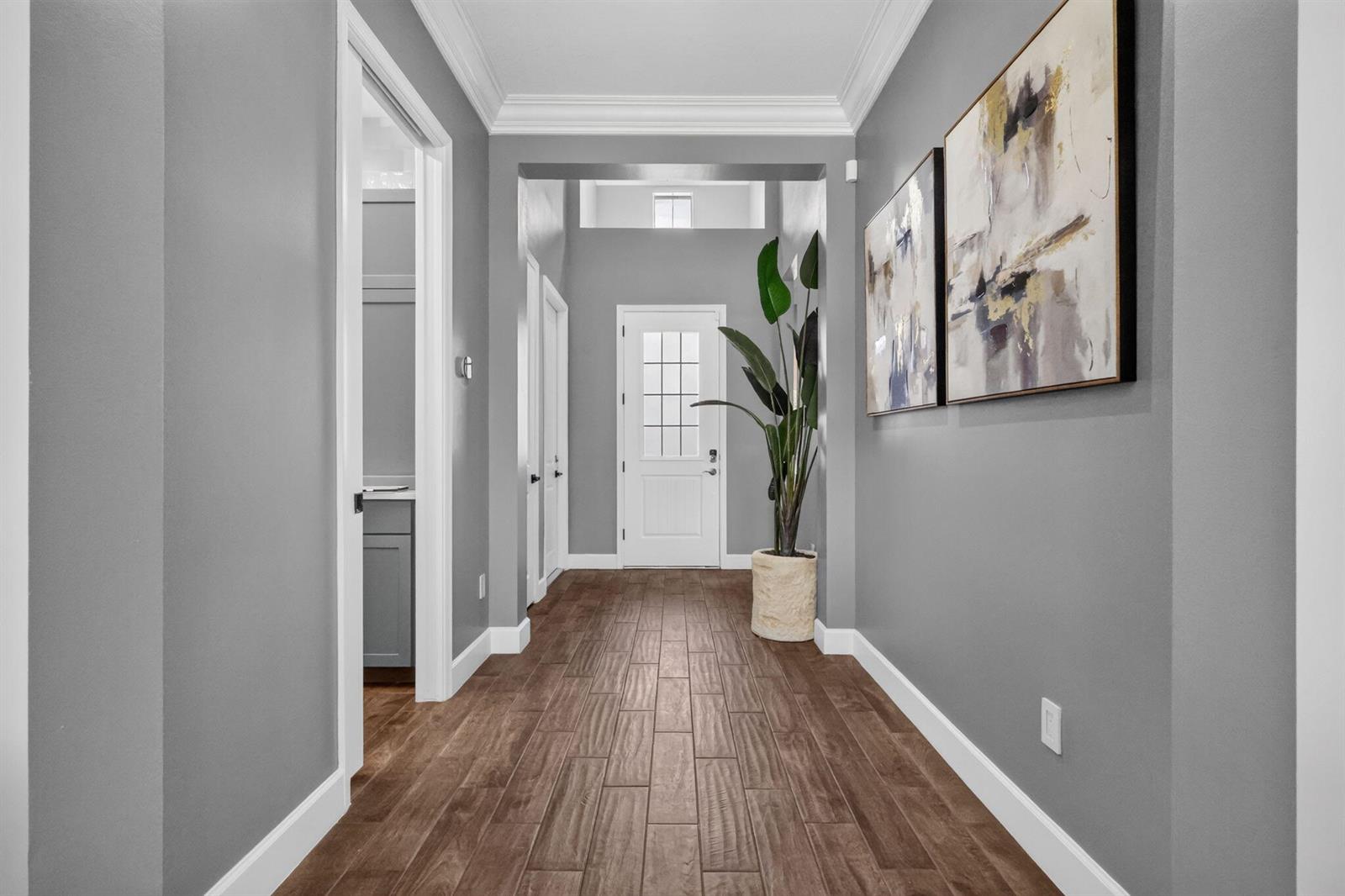 A hallway with gray walls, wood-look tile flooring, and two framed abstract paintings — 15660 Goldfinch Circle, FL 33470, FL