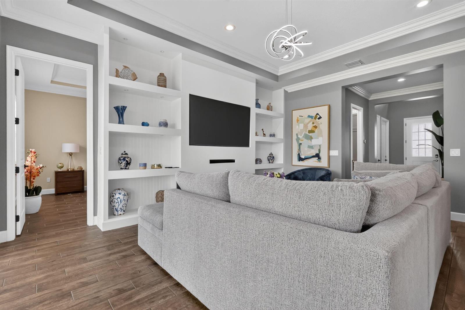 A living room features a large gray sectional sofa, built-in white shelving, and wood-look flooring — 15660 Goldfinch Circle, FL 33470, FL