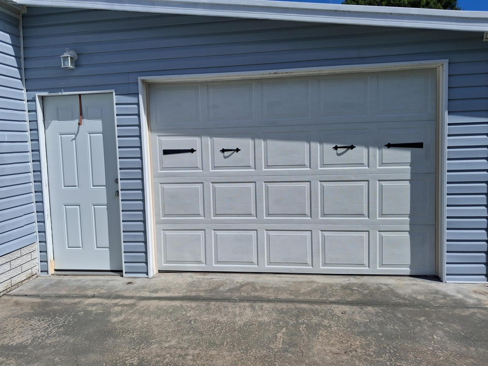 A blue-sided garage exterior featuring a white pedestrian door and a white sectional garage door — 1555 SW 35 Circle, Okeechobee FL 34974, OKEECHOBEE, FL