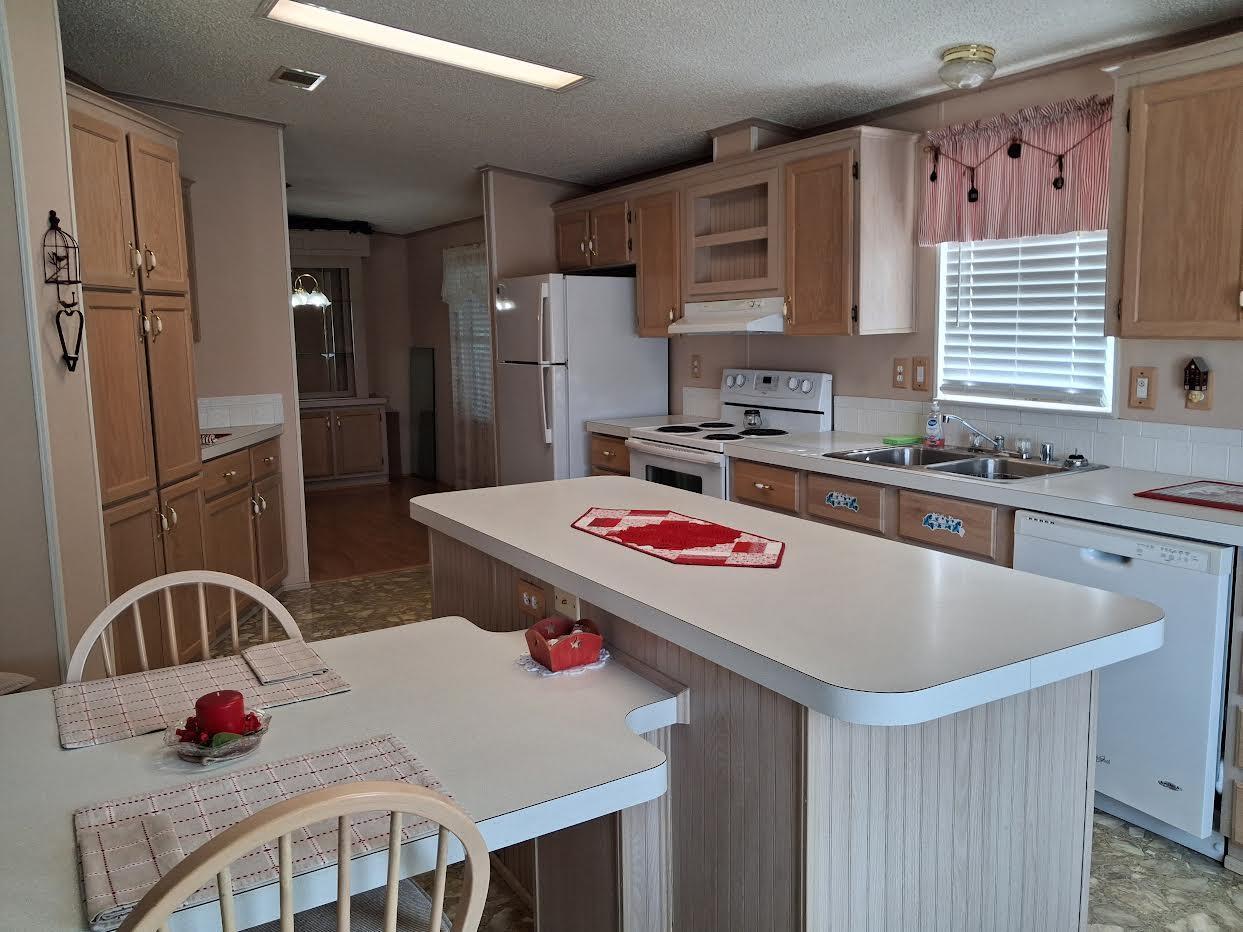 A kitchen features light wood cabinets, white appliances, a central island, and an attached dining table — 1555 SW 35 Circle, Okeechobee FL 34974, OKEECHOBEE, FL