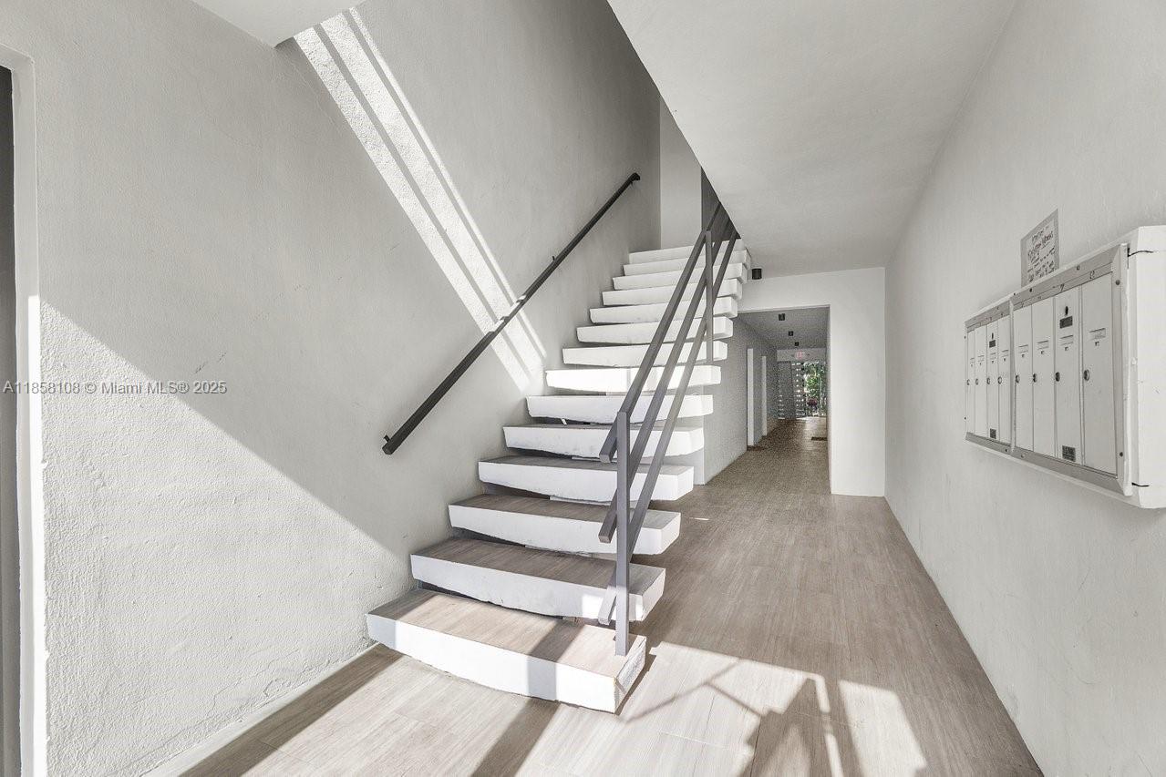 A staircase with white treads and a metal railing sits in a bright hallway — 1530 Crescent Cir, West Palm Beach FL 33403, WEST PALM BEACH, FL