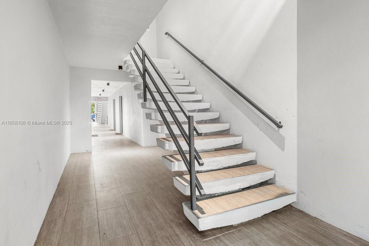 A staircase with light wood treads and a dark metal railing sits in a hallway — 1530 Crescent Cir, West Palm Beach FL 33403, WEST PALM BEACH, FL