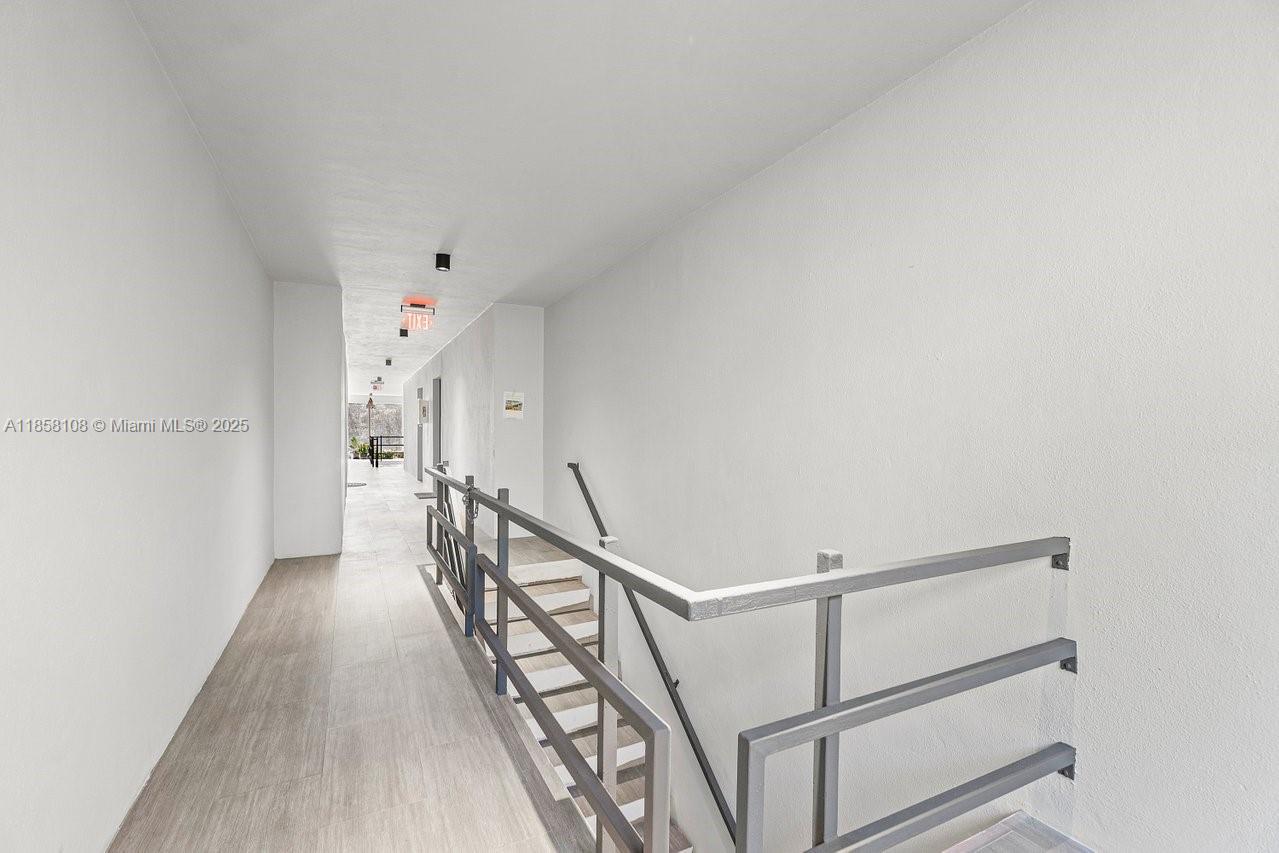 A long hallway features light wood-look flooring, white walls, and a metal stair railing — 1530 Crescent Cir, West Palm Beach FL 33403, WEST PALM BEACH, FL
