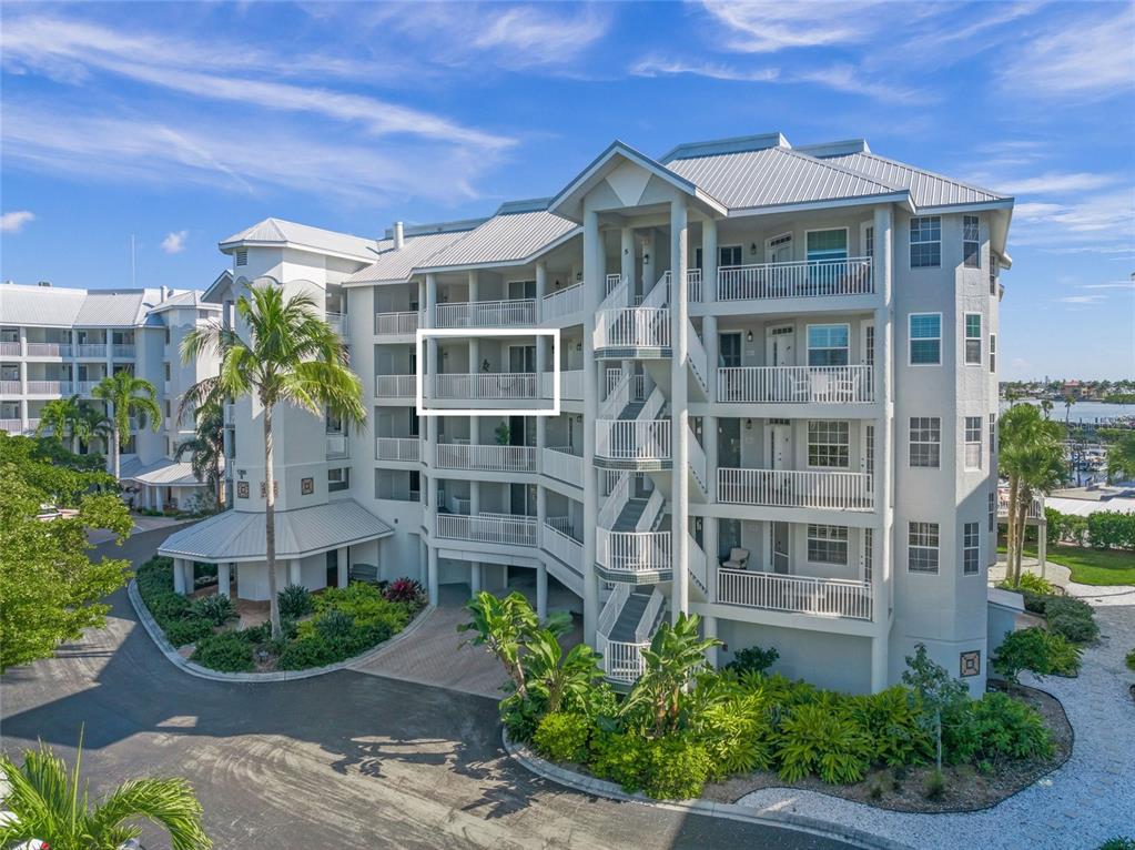 An exterior view of a multi-story apartment building featuring balconies and a central staircase — 1260 DOLPHIN BAY WAY UNIT 403, SARASOTA, FL