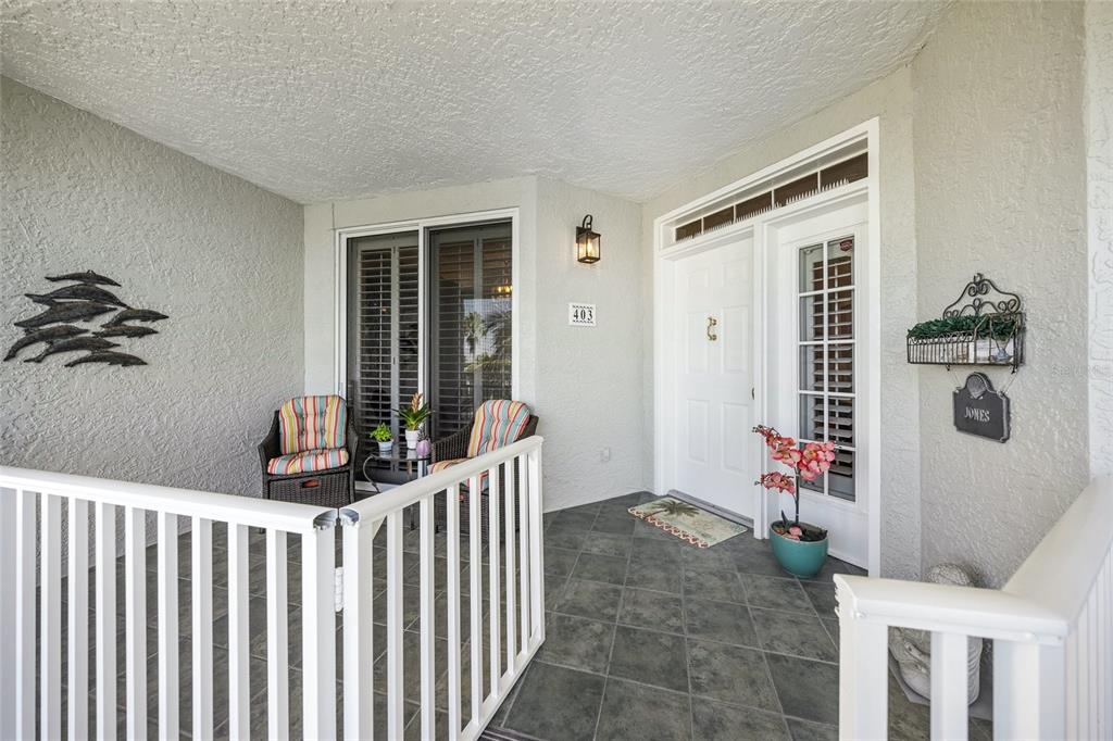 A covered entryway features a tiled floor, white railings, a front door, and patio seating — 1260 DOLPHIN BAY WAY UNIT 403, SARASOTA, FL