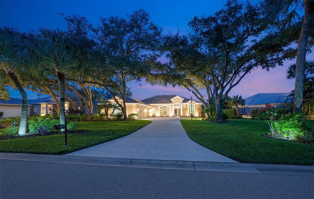 A single-story house with a concrete driveway and mature trees at dusk — 11 N CAYMAN ISLES BOULEVARD, ENGLEWOOD, FL