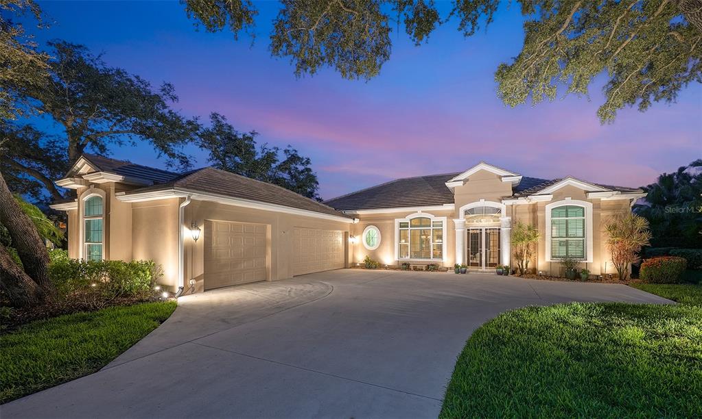A single-story beige house with a three-car garage and a large concrete driveway at dusk — 11 N CAYMAN ISLES BOULEVARD, ENGLEWOOD, FL