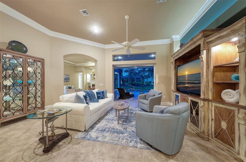 A living room features a white sofa, two armchairs, a television unit, and pool views — 11 N CAYMAN ISLES BOULEVARD, ENGLEWOOD, FL
