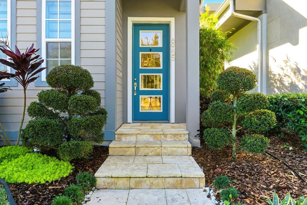 A blue front door with four glass panels is centered above stone steps and landscaping — 6955 HIGGS ALLEY, ORLANDO, FL