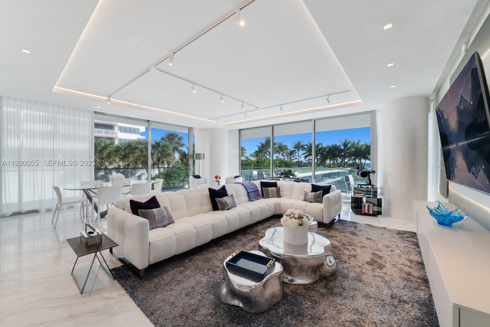 A modern living room features a white sectional sofa, metallic coffee tables, and floor-to-ceiling windows — 10203 Collins Ave # 201, Bal Harbour FL 33154, BAL HARBOUR, FL
