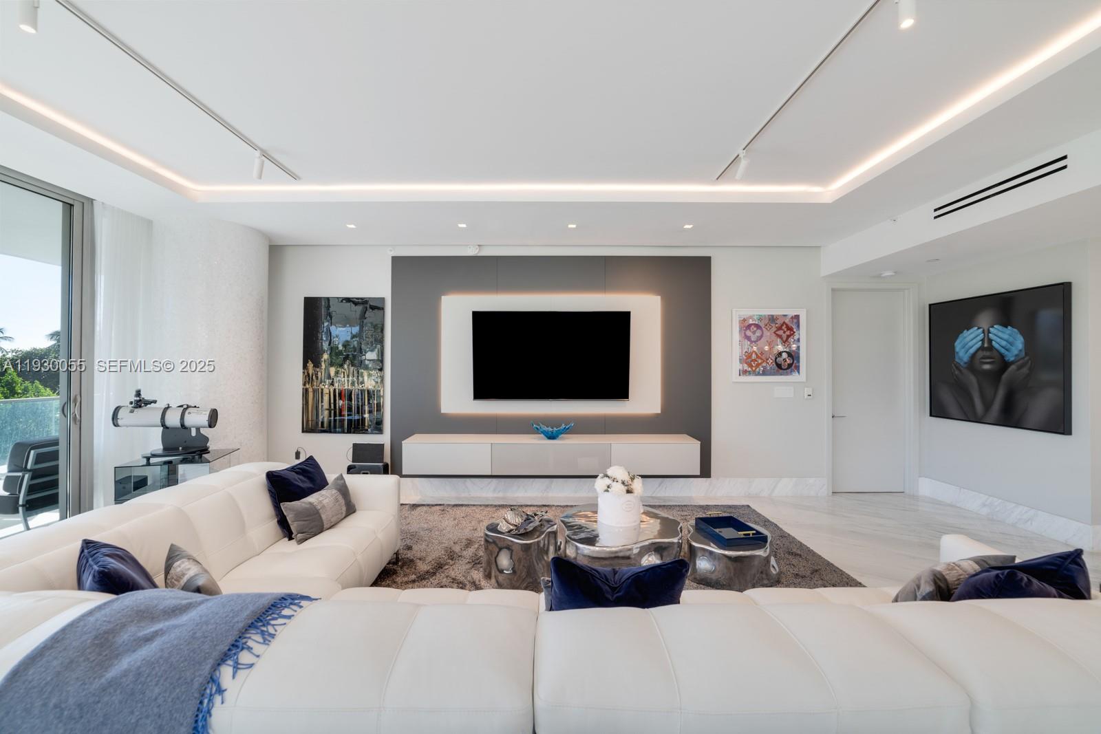A modern living room features a white sectional sofa, a wall-mounted television, and metallic tables — 10203 Collins Ave # 201, Bal Harbour FL 33154, BAL HARBOUR, FL