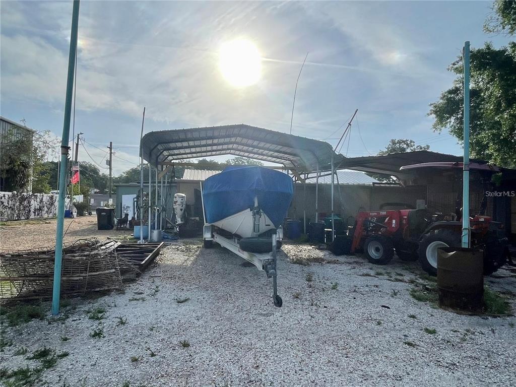 A boat on a trailer sits under a metal carport next to a red tractor — 5101 W INGRAHAM STREET, TAMPA, FL