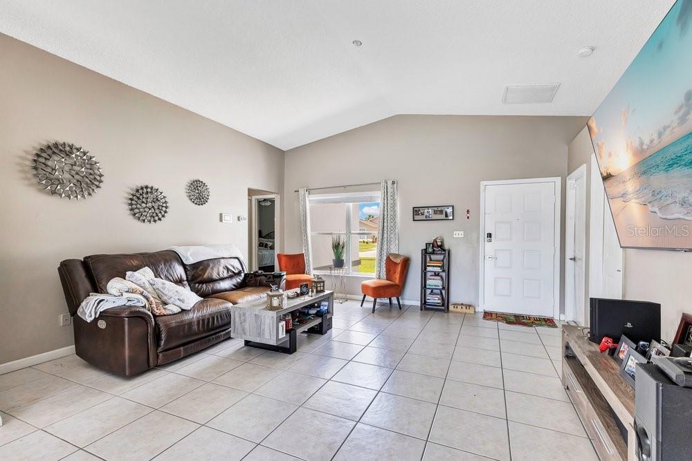 A living room with tile flooring, a brown leather sofa, and a wall-mounted television — 3130 KOVAL COURT, ORLANDO, FL